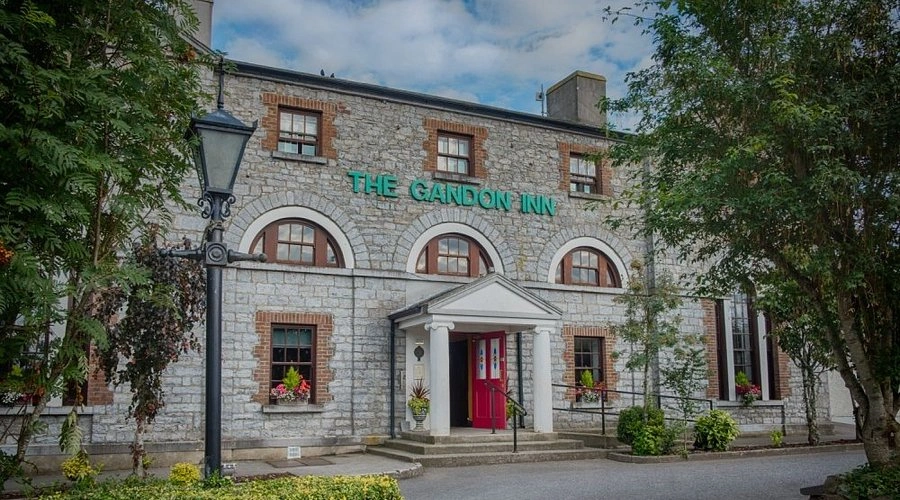 The Gandon Inn, featuring a charming stone façade and arched windows, welcomes guests with vibrant flowers and a distinct entrance.