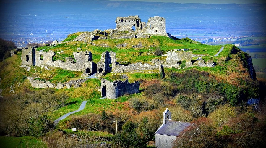 Ruins of the Rock of Dunamase on a grassy hill, with countryside views and a small chapel below.