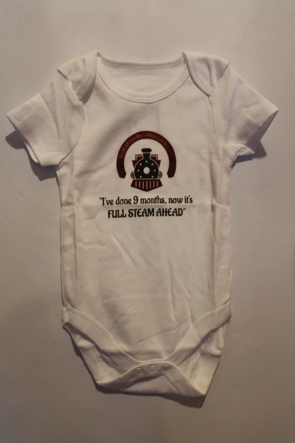 White baby bodysuit featuring the phrase, "I've done 9 months, now it's FULL STEAM AHEAD," alongside a graphic of a steam train, celebrating the journey of pregnancy and the arrival of a new baby.