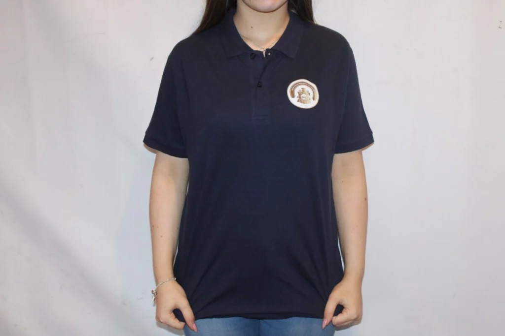 Navy polo shirt worn by a woman, featuring a distinctive logo on the left chest. The background is plain and light to highlight the shirt's design.
